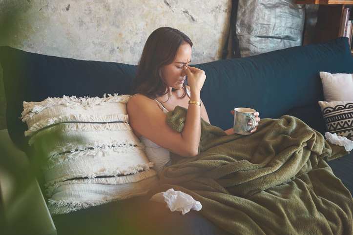 Woman pinching nose on couch.Cold and flu concept.
